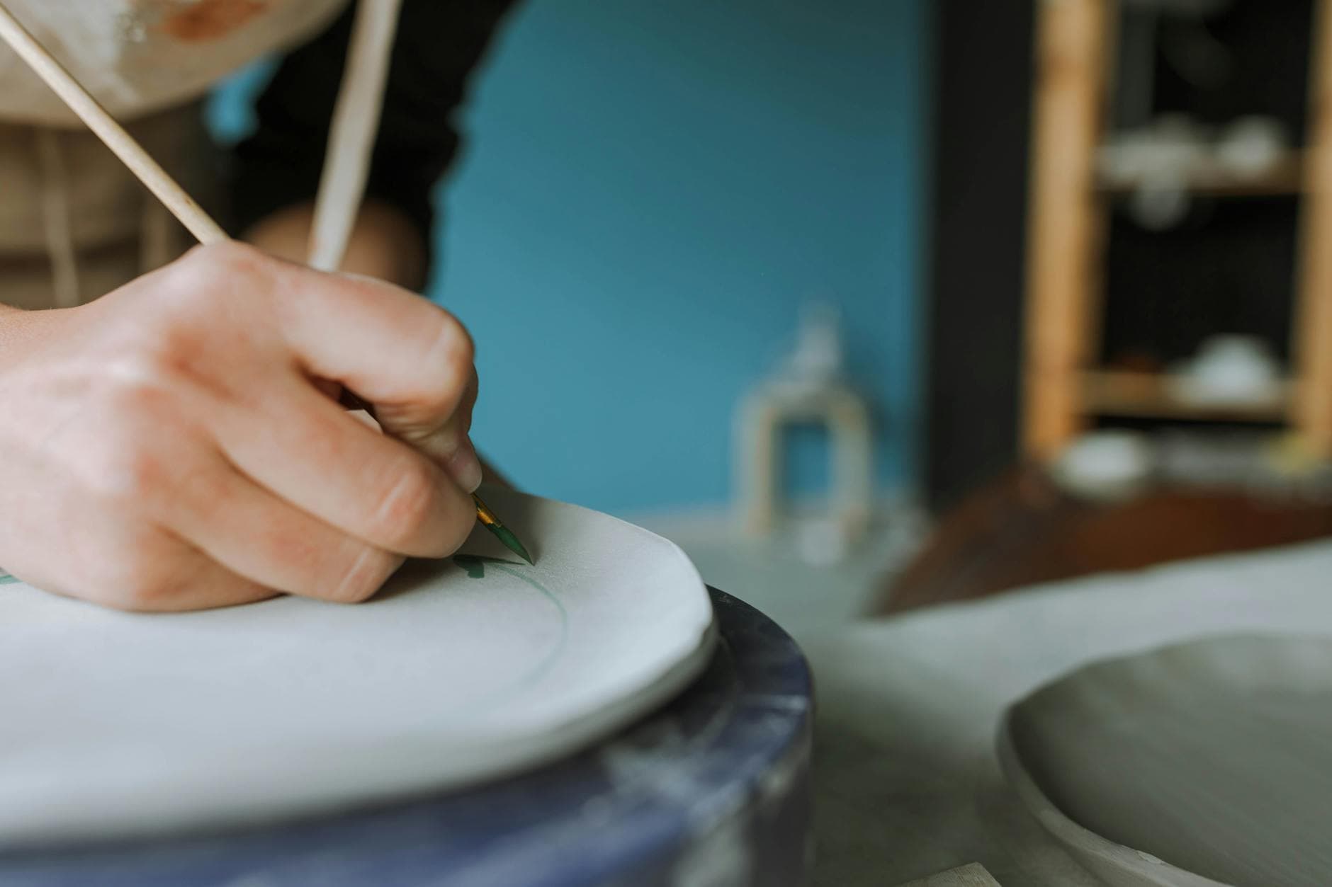 A close-up shot of a person painting pottery with a brush in a ceramics studio, displaying artistic focus.